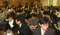 写真�D：種田憲一郎さん（国立保健医療科学院政策科学部主任研究官）の音頭取りで、会場一杯の参加者が「医師」と「家族」のペアになってロールプレイ