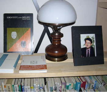 写真�@：英文の博士論文（左）とお気に入りのランプと並んで、在りし日の外山義さんの写真が